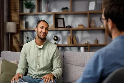 Two men converse while sitting on a couch, showcasing a moment of dialogue and connection between them.