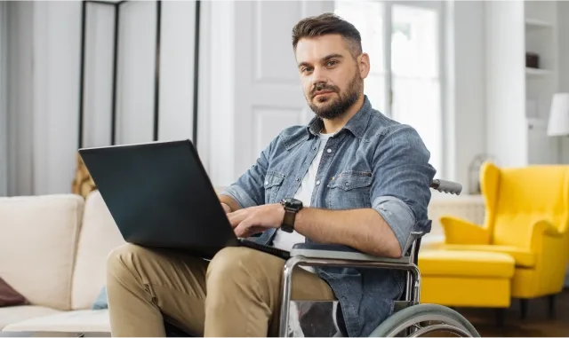 A man in a wheelchair is focused on using a laptop, showcasing accessibility and technology in everyday life.