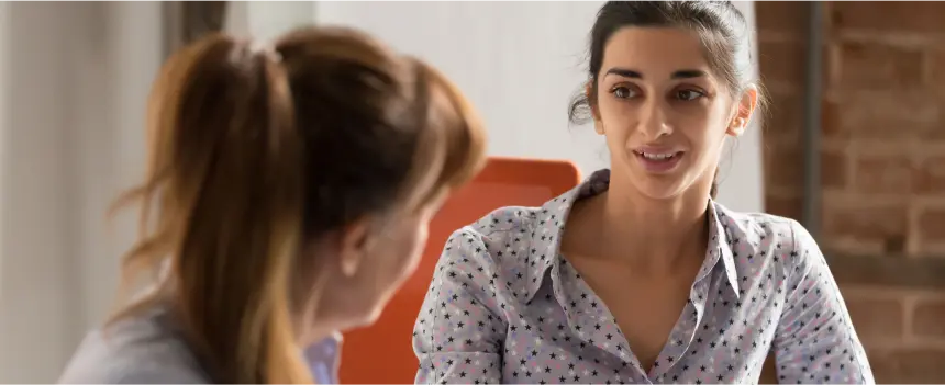 A woman engages in conversation with another woman in a professional office setting, showcasing collaboration and communication.