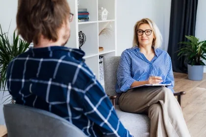 A woman seated in a chair engages in conversation with a man, both appearing attentive and engaged in dialogue.