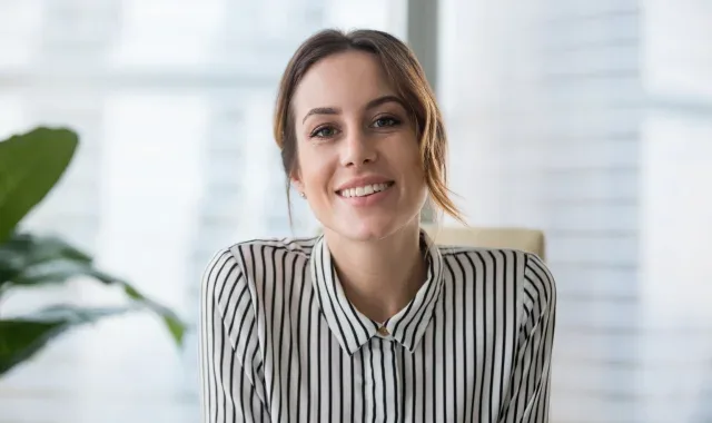 A woman smiling warmly while seated at her desk in a professional office environment, exuding positivity and confidence.