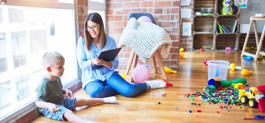 A woman and a child are seated on the floor, engaged in play with various colorful toys scattered around them.