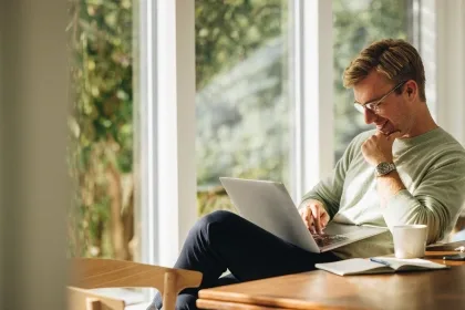 A man seated at a table, working on a laptop while enjoying a cup of coffee.