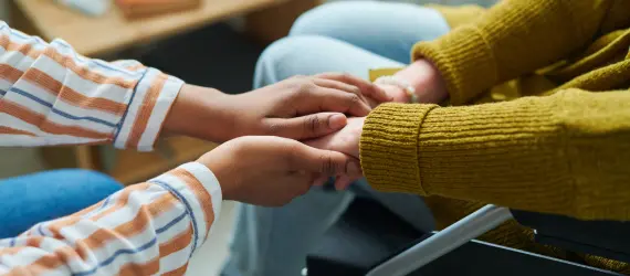 two people sitting down as one embraces the hands of the other.