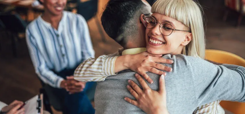 In a meeting room, a woman hugs a man, symbolizing camaraderie and connection in a professional setting.