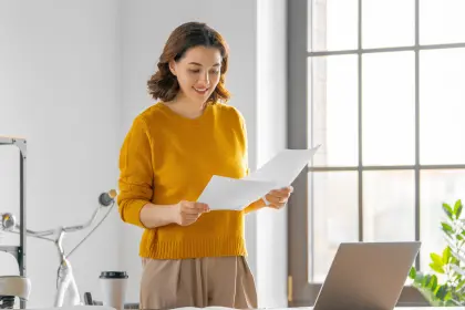 A beautiful young woman attentively reading a document in her well-organized office space.