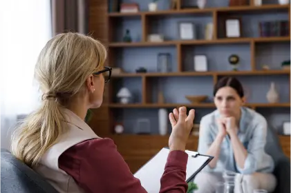 A woman engages in conversation with another woman in a professional meeting room setting.