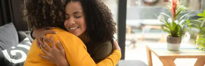 In a comfortable living room, two women share a heartfelt hug, conveying warmth and friendship in their embrace.