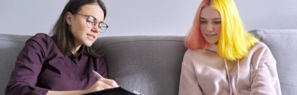 Two women with colorful hair are comfortably sitting on a couch, enjoying each other's company in a cozy setting.